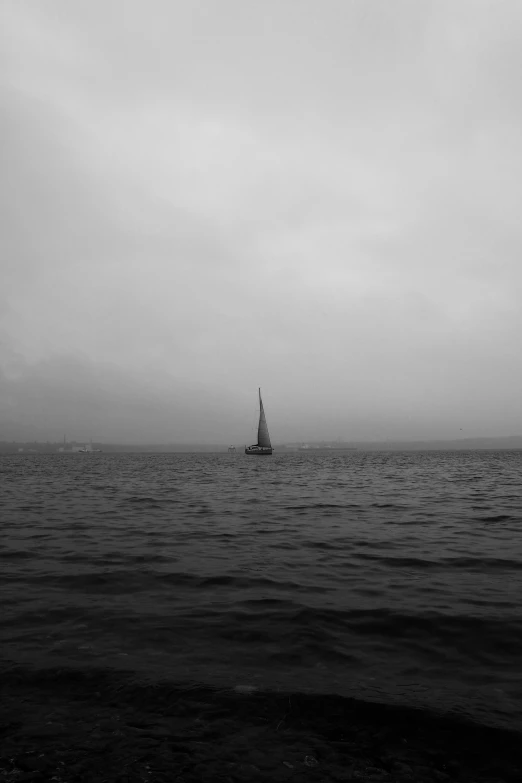 a lone sail boat on the ocean in the rain