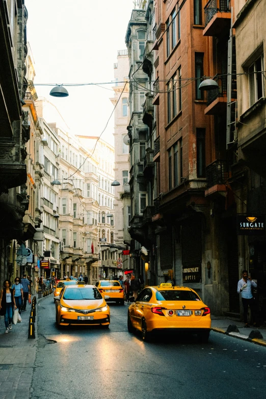 a city with people on a sidewalk and taxi cabs