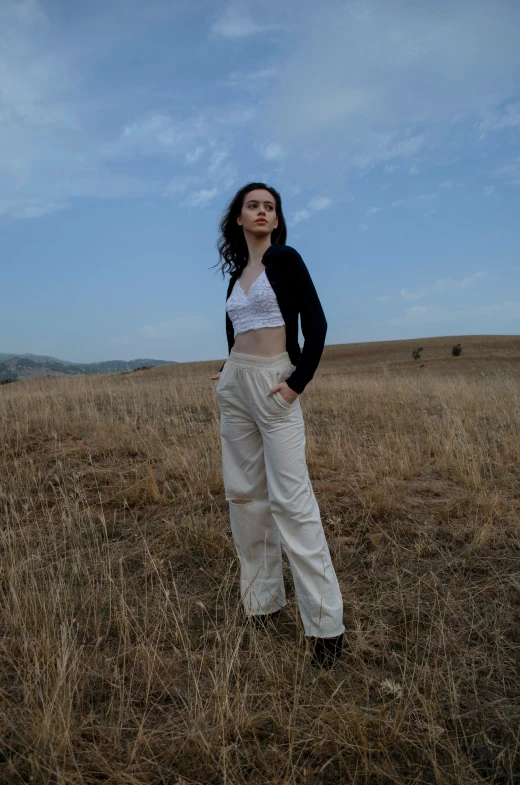 a woman posing in the middle of a field wearing white and black clothes