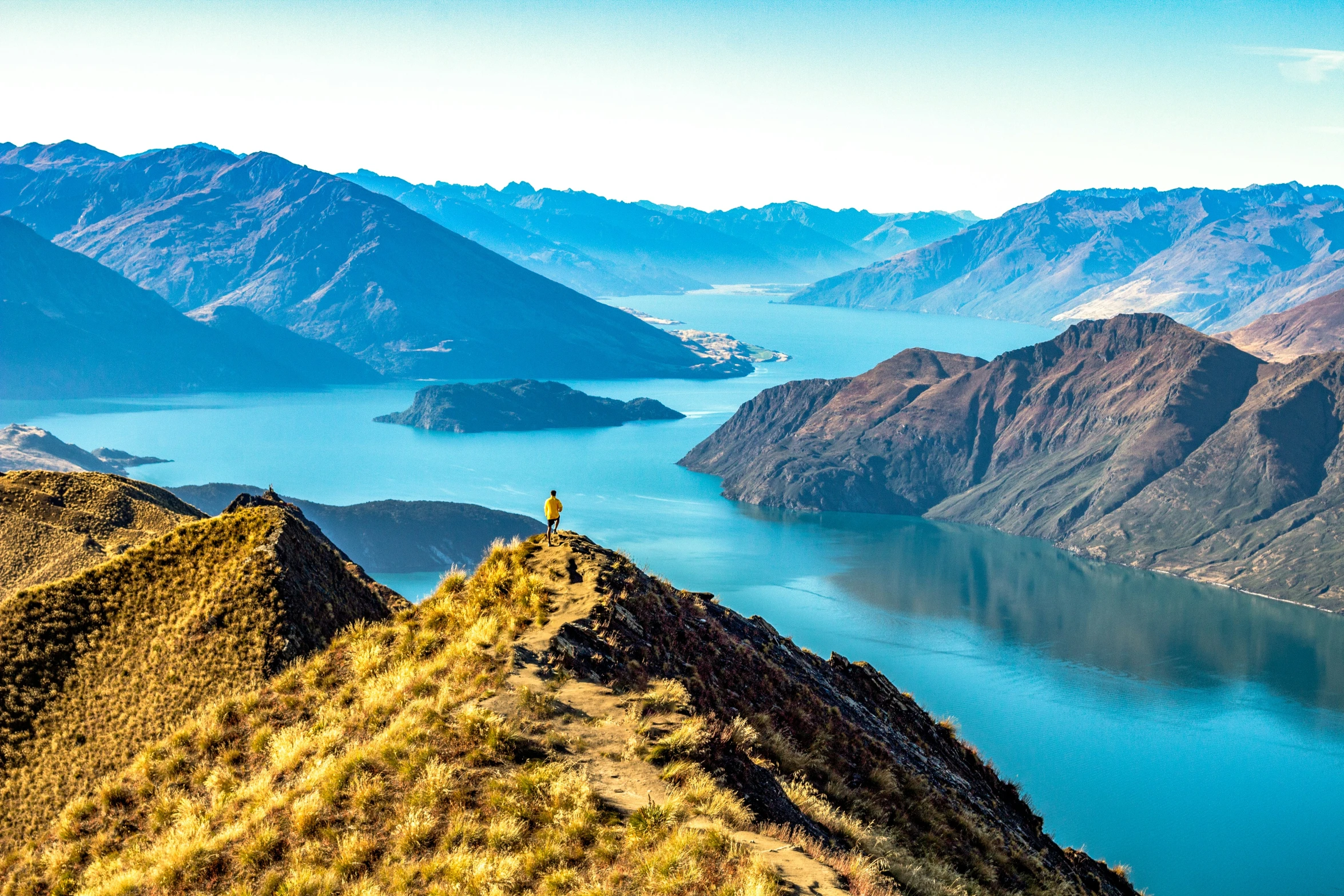 a hiker standing on a cliff on the side of a mountain looking out at a lake