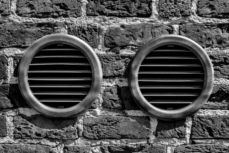 two round windows in black and white against a brick wall