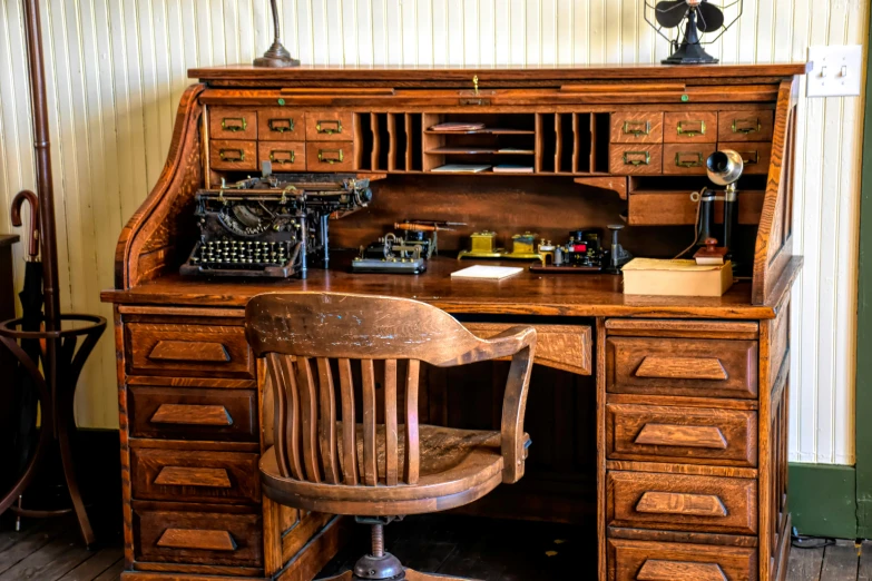 an old desk with some typewriter, lamp and chair on top