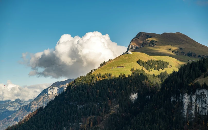 a green grassy hill with mountains and clouds in the background