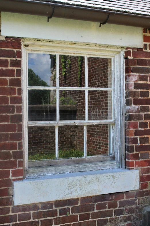 an old brick building that has a window on one side and a small brick house and water in the other