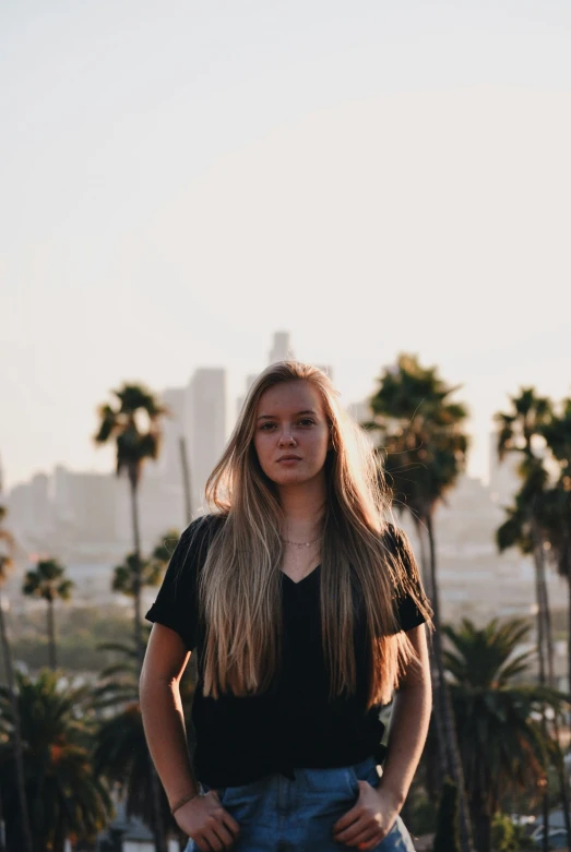 girl standing on sidewalk with palm trees and city in background