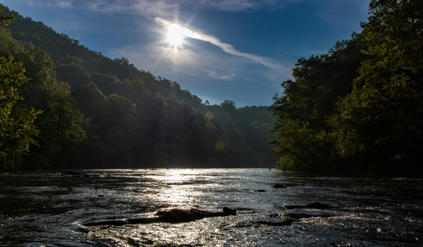 the sun shines over a river and the trees in the distance