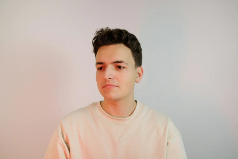 a man standing against a wall in a white sweater