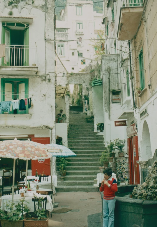 a man walking through an alleyway with outdoor tables and umbrellas