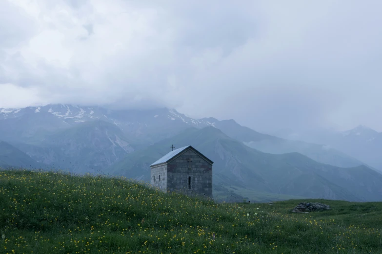 an old building sitting on the side of a hill with mountains in the background