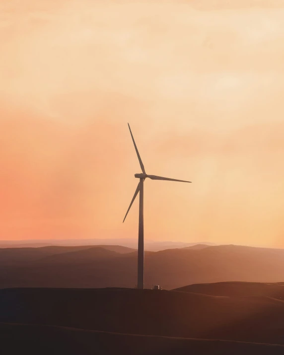 a windmill near a hill in the sunset