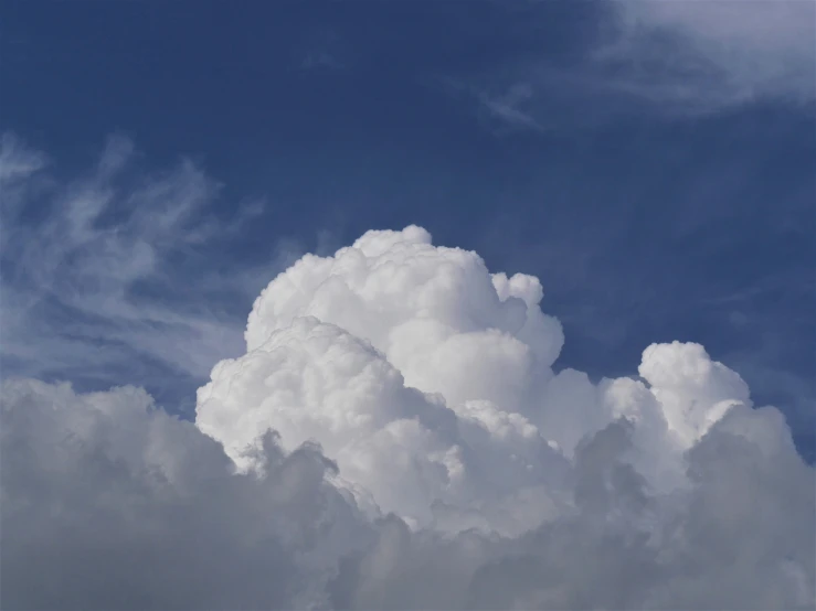 a huge cloud in the sky with a plane flying below it