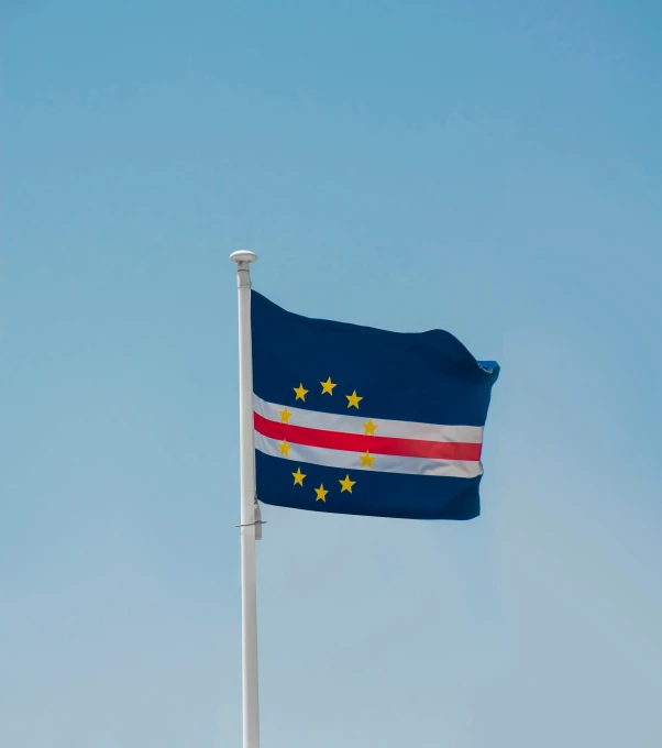 a tall flag waving in the wind against a blue sky