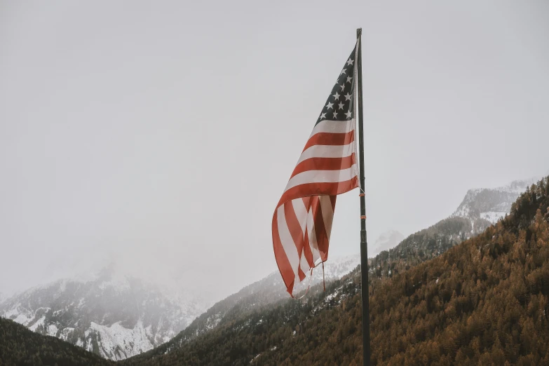 a flag waving in the wind near a mountain range