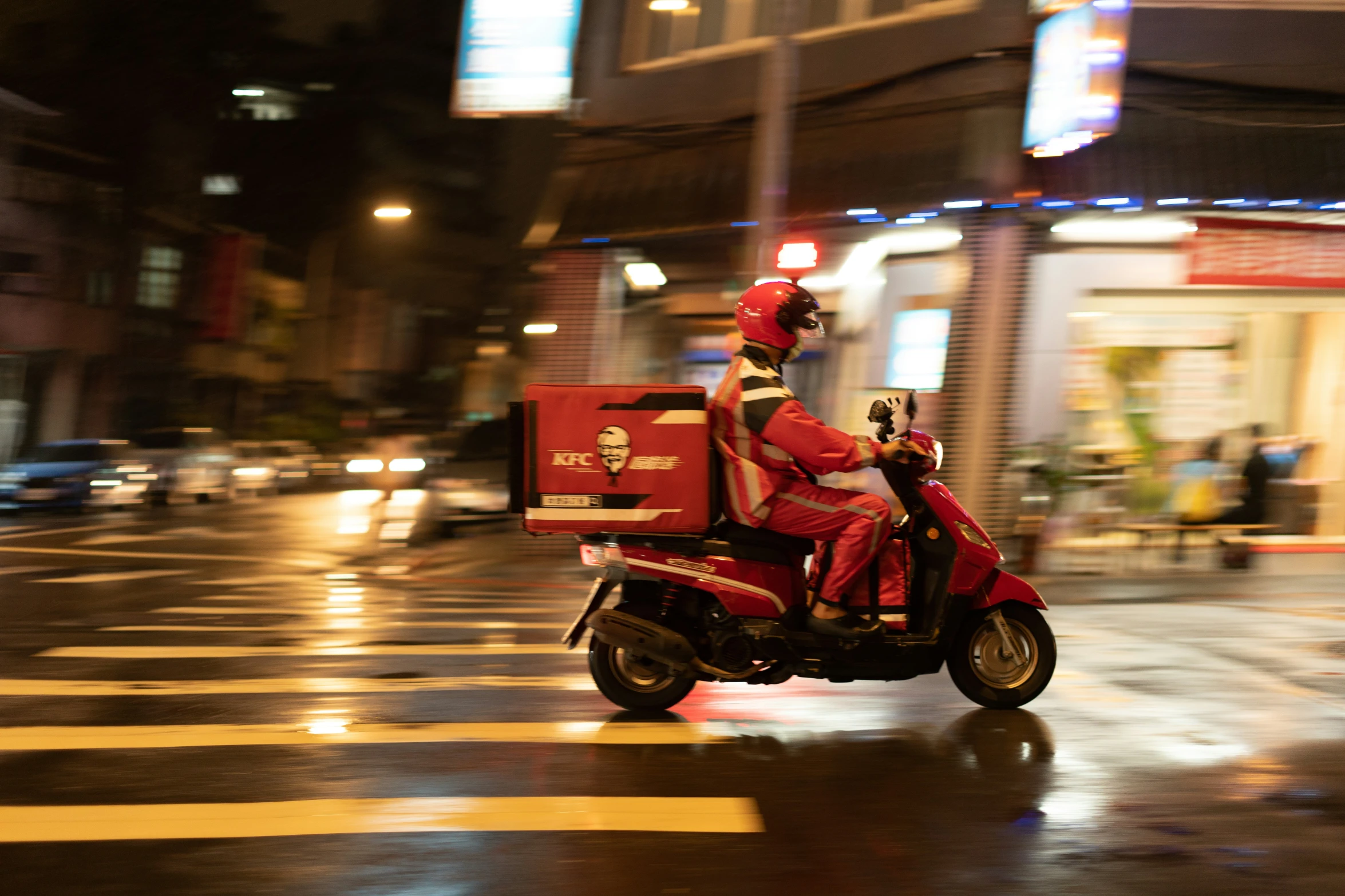 a person riding a motor scooter down a rain soaked street