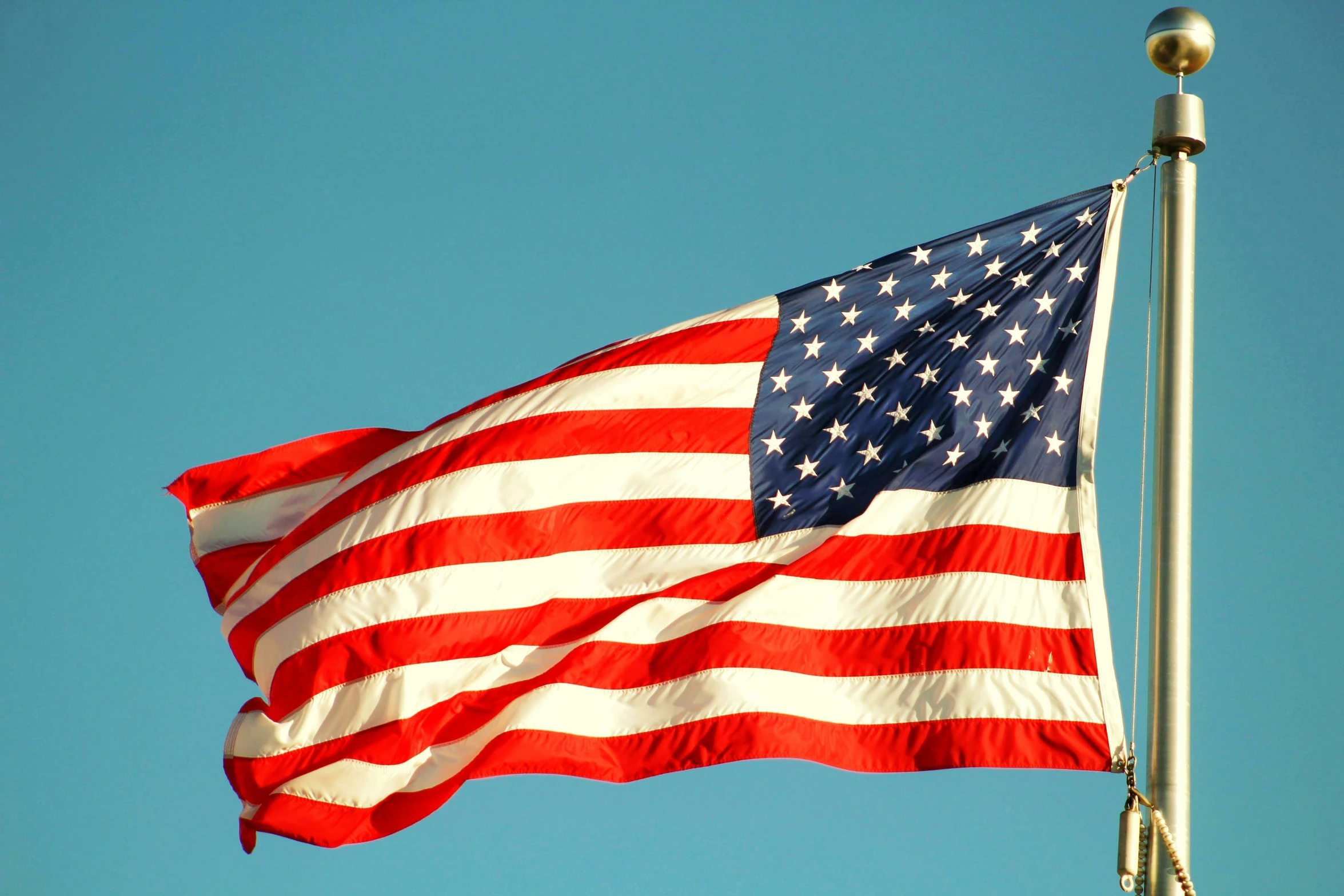 a us flag waving in the wind with blue sky behind