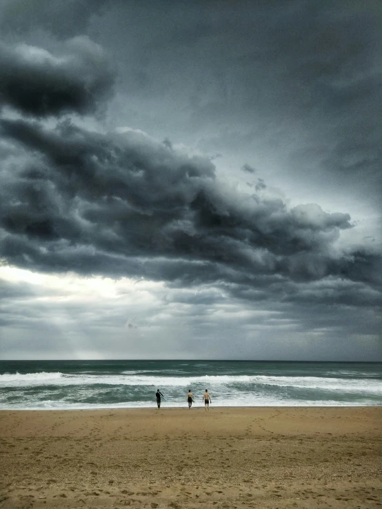 two people walk along the beach with a stormy sky in the background