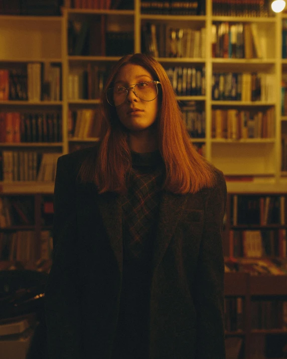 woman with red hair and glasses looking at camera in room full of books