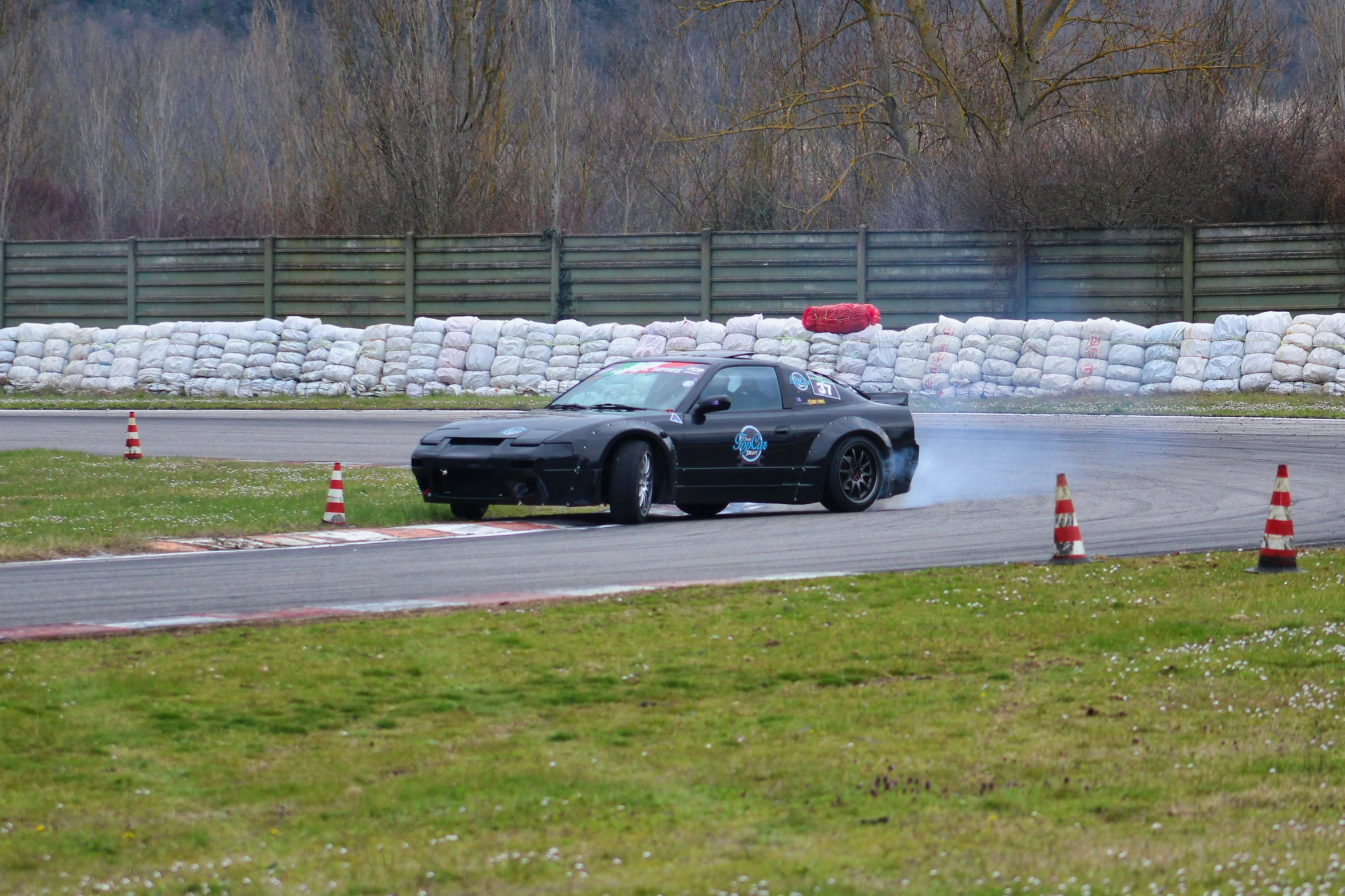 a car doing a burn driving on a track with cones on both sides