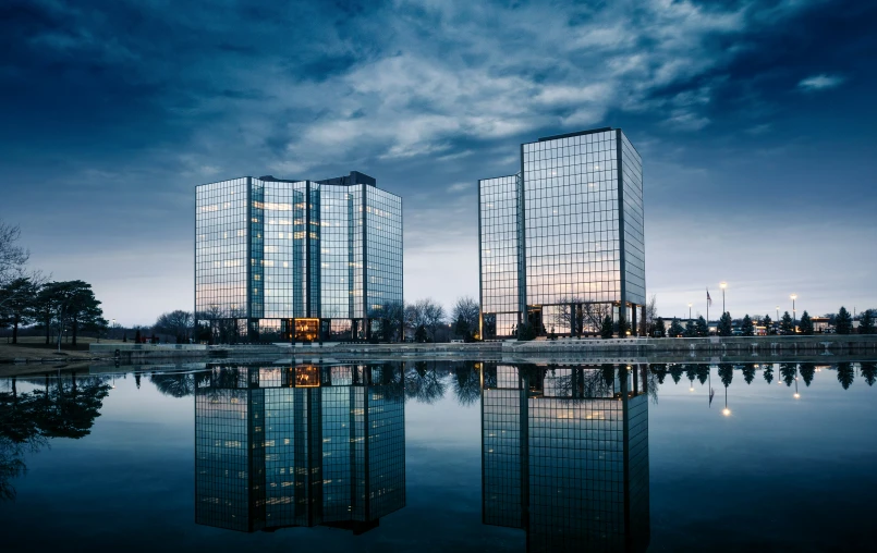 two skyscrs reflecting in the water with other tall buildings