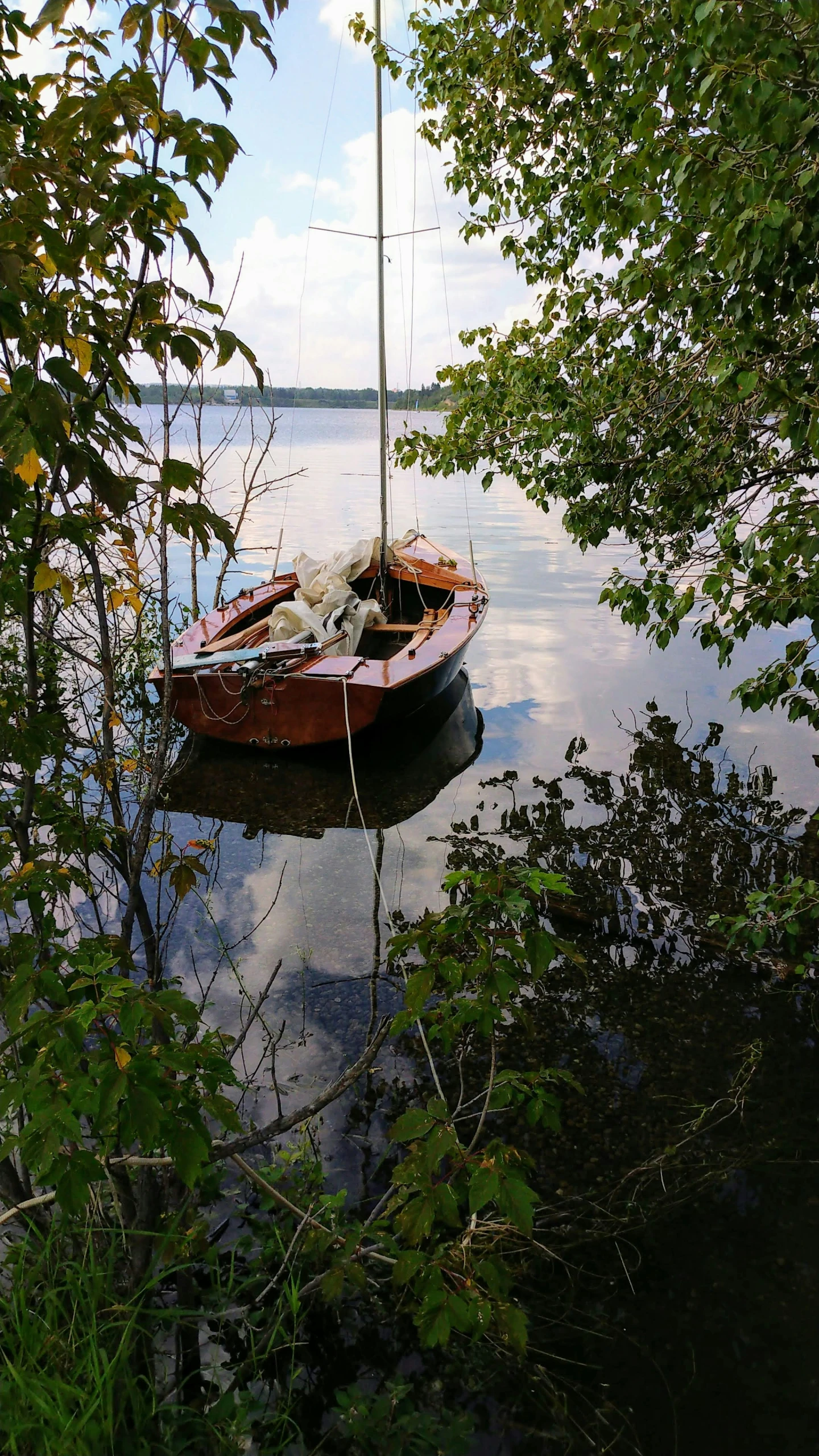 a small boat with mast docked in water