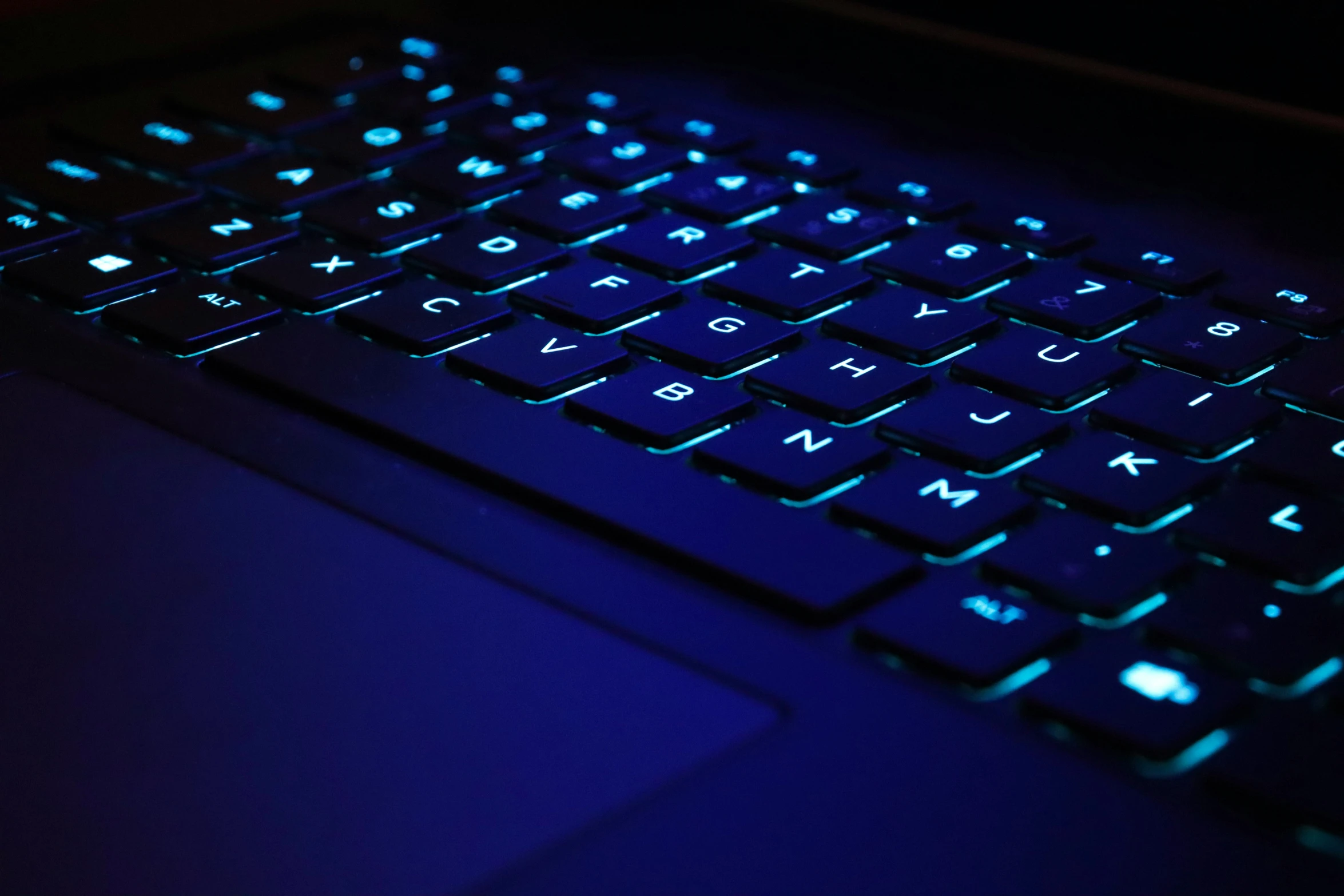 closeup of a blue illuminated keyboard with its dark back ground