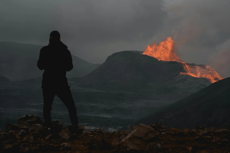 a man in black jacket looking at volcano on hill