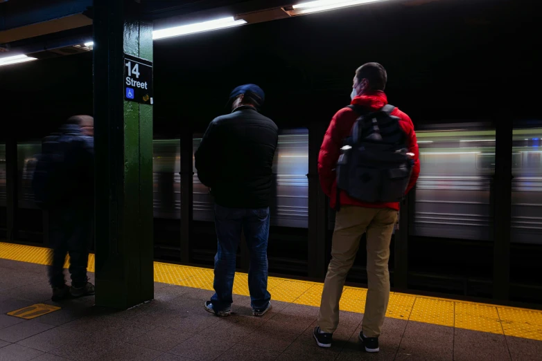 two men stand in a subway station as a train comes in