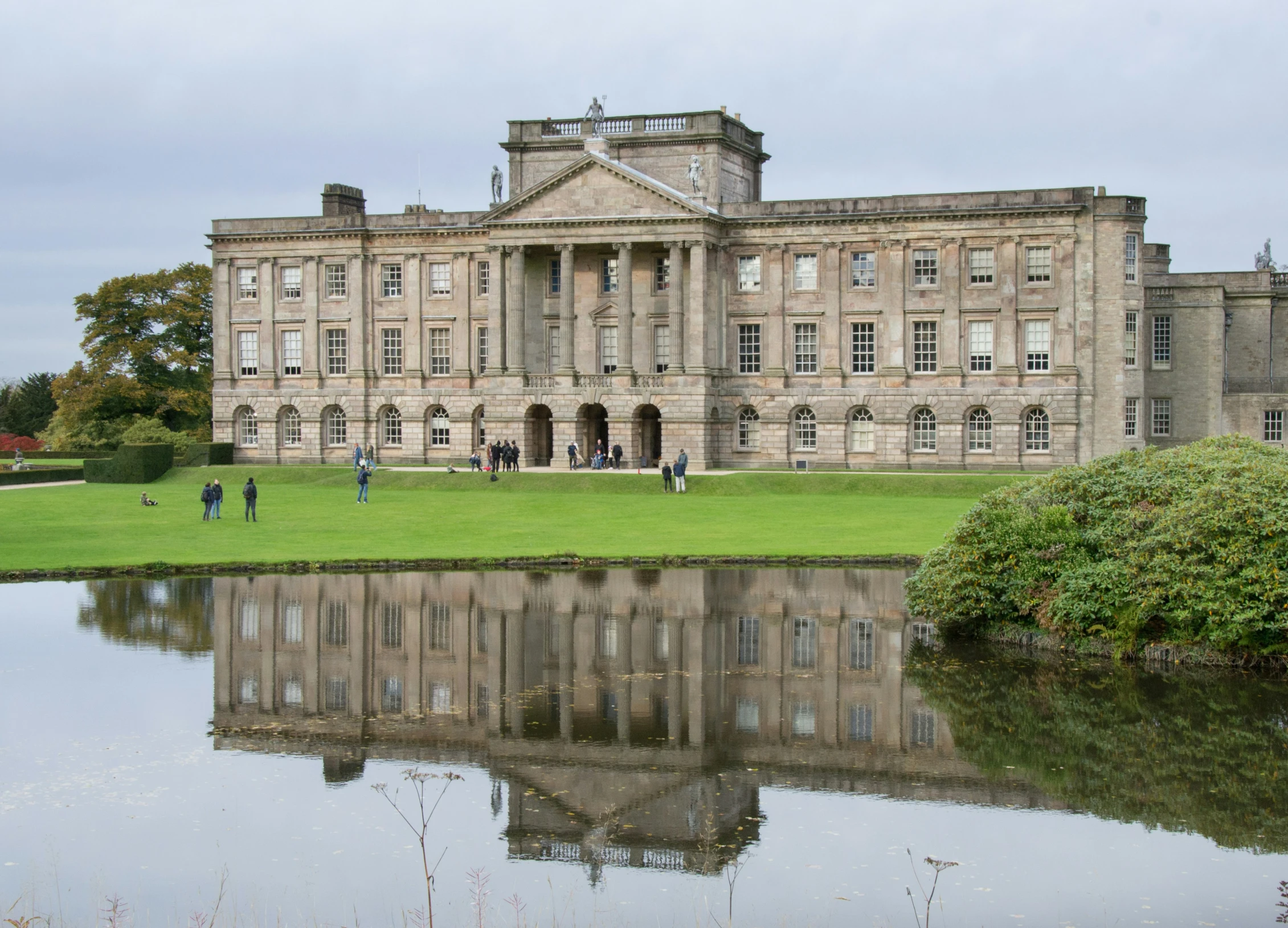 large, old building with lots of windows on a grassy area with water and trees