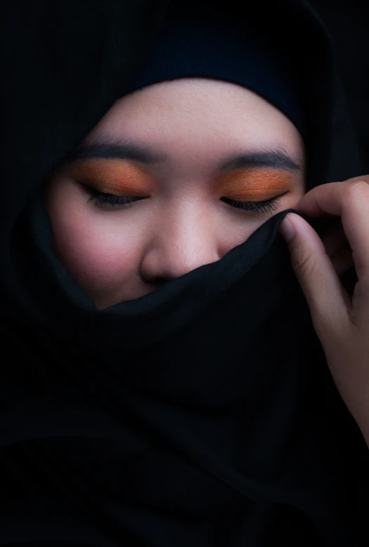 a young person with orange makeup wearing a black headscarf