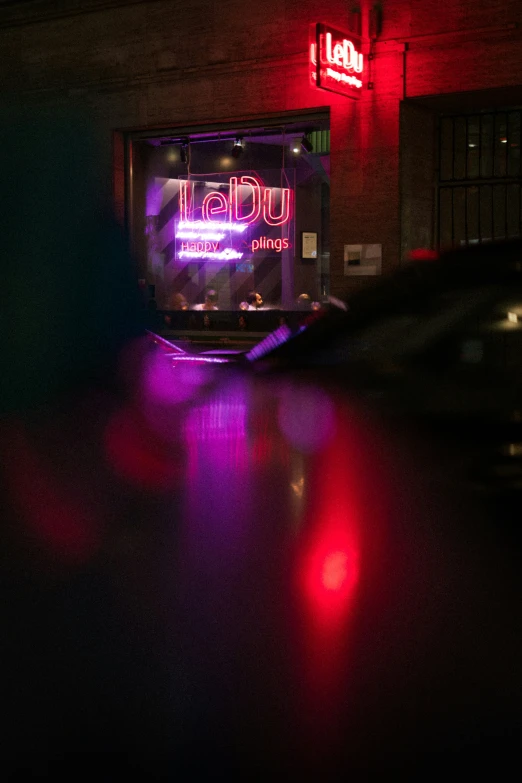 a neon bar sign and some parked cars at night