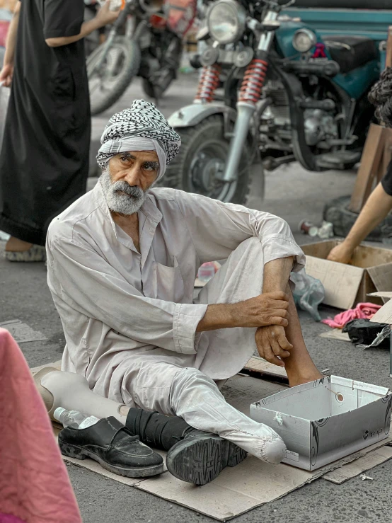 an old man with a beard wearing a hat sits on the ground