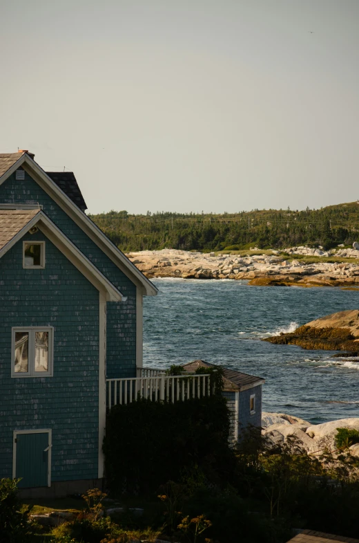 a blue house next to the ocean with a boat on the water