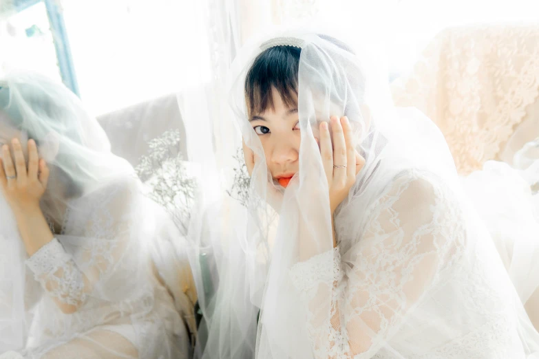 an asian woman in a lace wedding dress covering her face