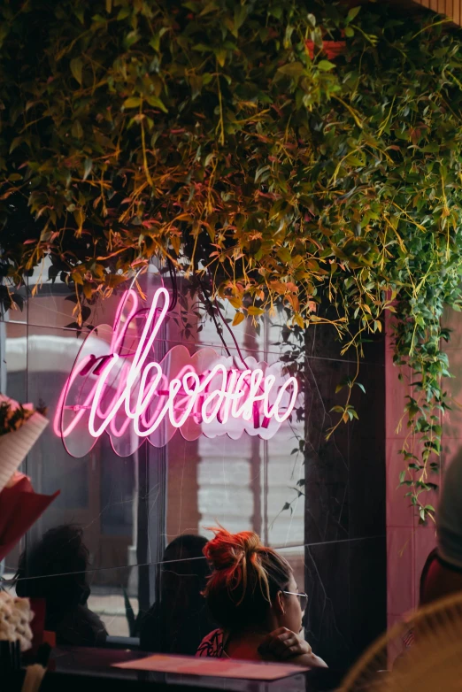 people sitting on a bench under a tree with neon signage