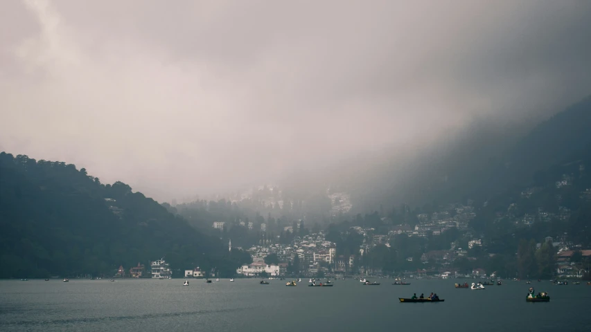 several small boats sailing down the ocean underneath gray skies