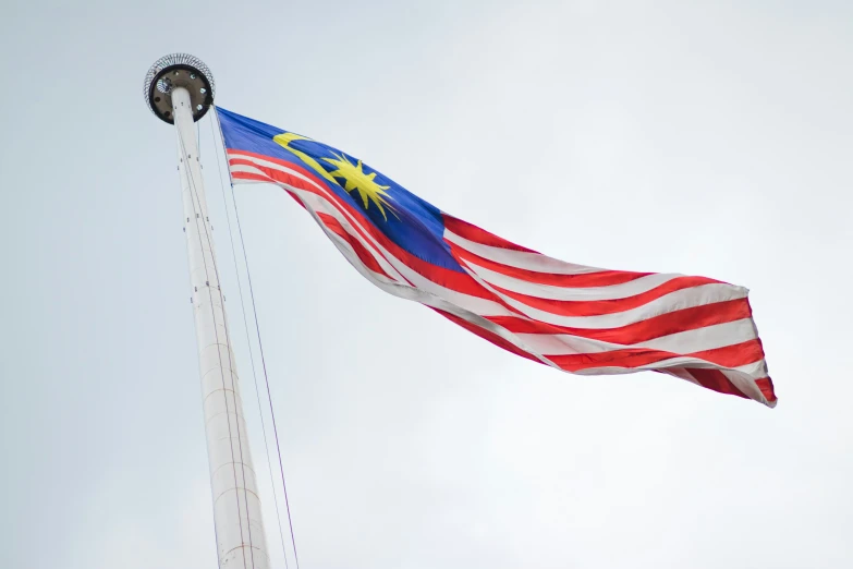 the malaysian and american flags waving from a metal pole