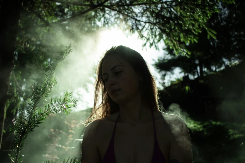 a woman is looking back while she stands in front of trees and smoke