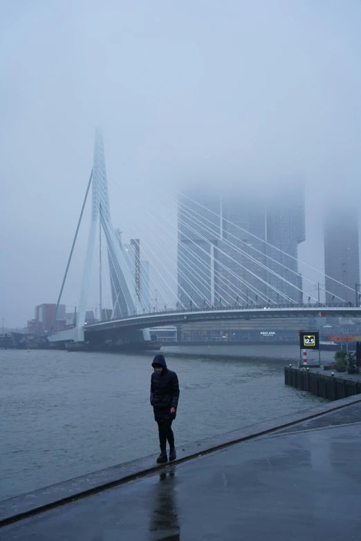 the person is standing by the water near the bridge