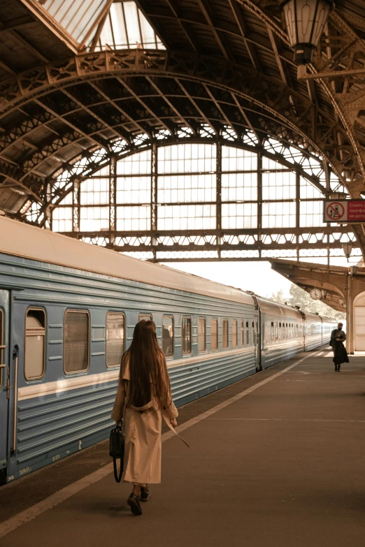 a woman walking through a railway station with a passenger train