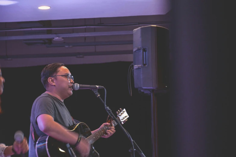 a man in glasses and a black t - shirt playing guitar