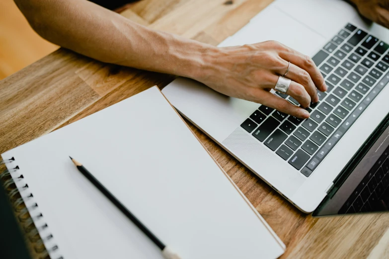 a hand with ring typing on the keyboard of a laptop