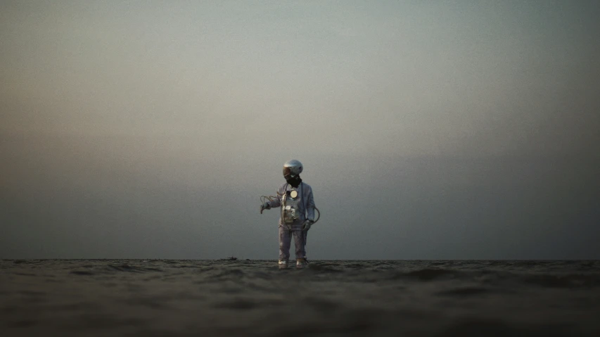 a person stands on a sand beach with their back to the camera, as the sky is grey