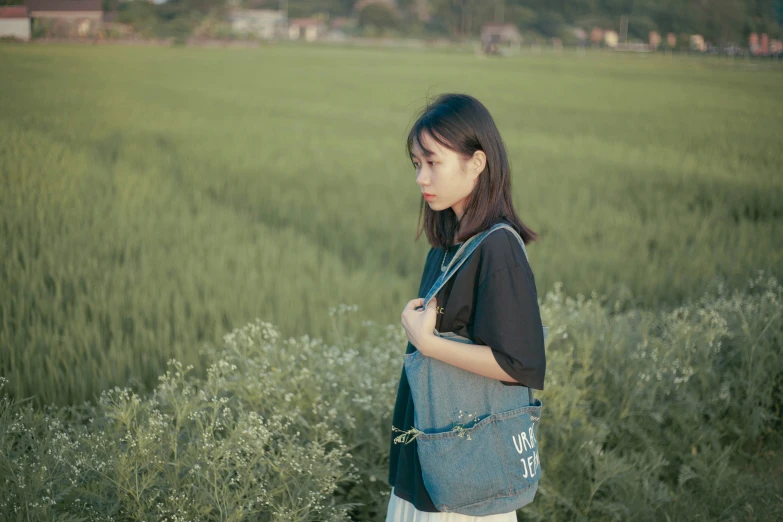 a young woman in a field carrying a blue purse