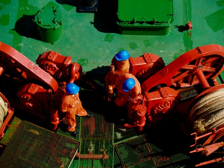 workers stand on a ship deck with red ships ropes