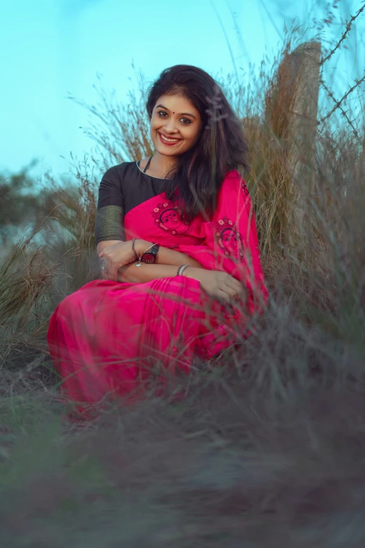 a beautiful young woman in a red sari sits in tall grass