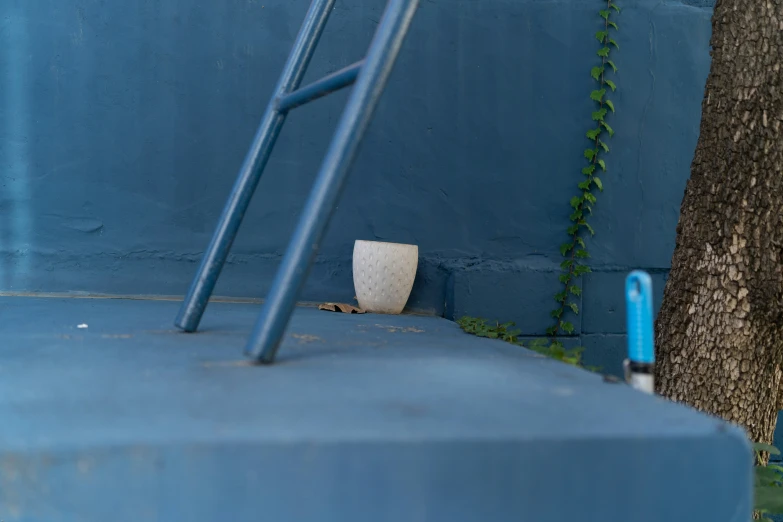 a blue wall with a white flower vase by it and a blue ladder beside the wall