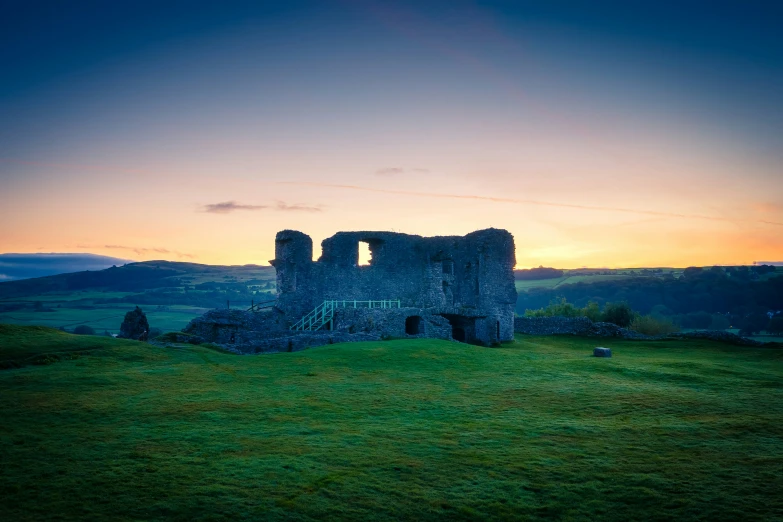 the remains of a castle and grass field at sunset