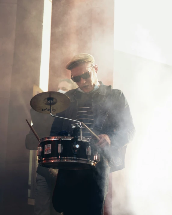 a man with glasses and a short hair plays drums