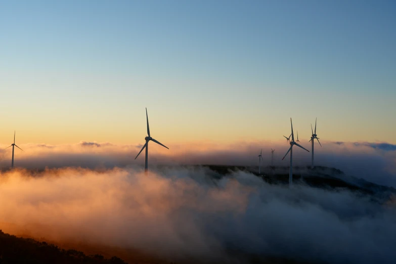 the three wind turbines are standing on top of the fog