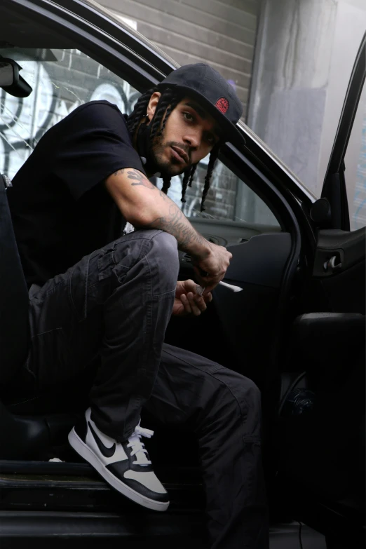a man sitting inside of his car with dreadlocks and a cap on